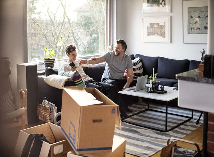 Photo of father and son in living room sitting on couch with moving boxes in foreground